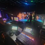 A dark TV Studio with a colourful set, and screens in the foreground