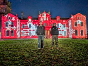 Warehouse Digital Directors, Pete and James standing in front of Hestercombe House. A Large stately home with the Warehouse Digital logo projected all over it at night.